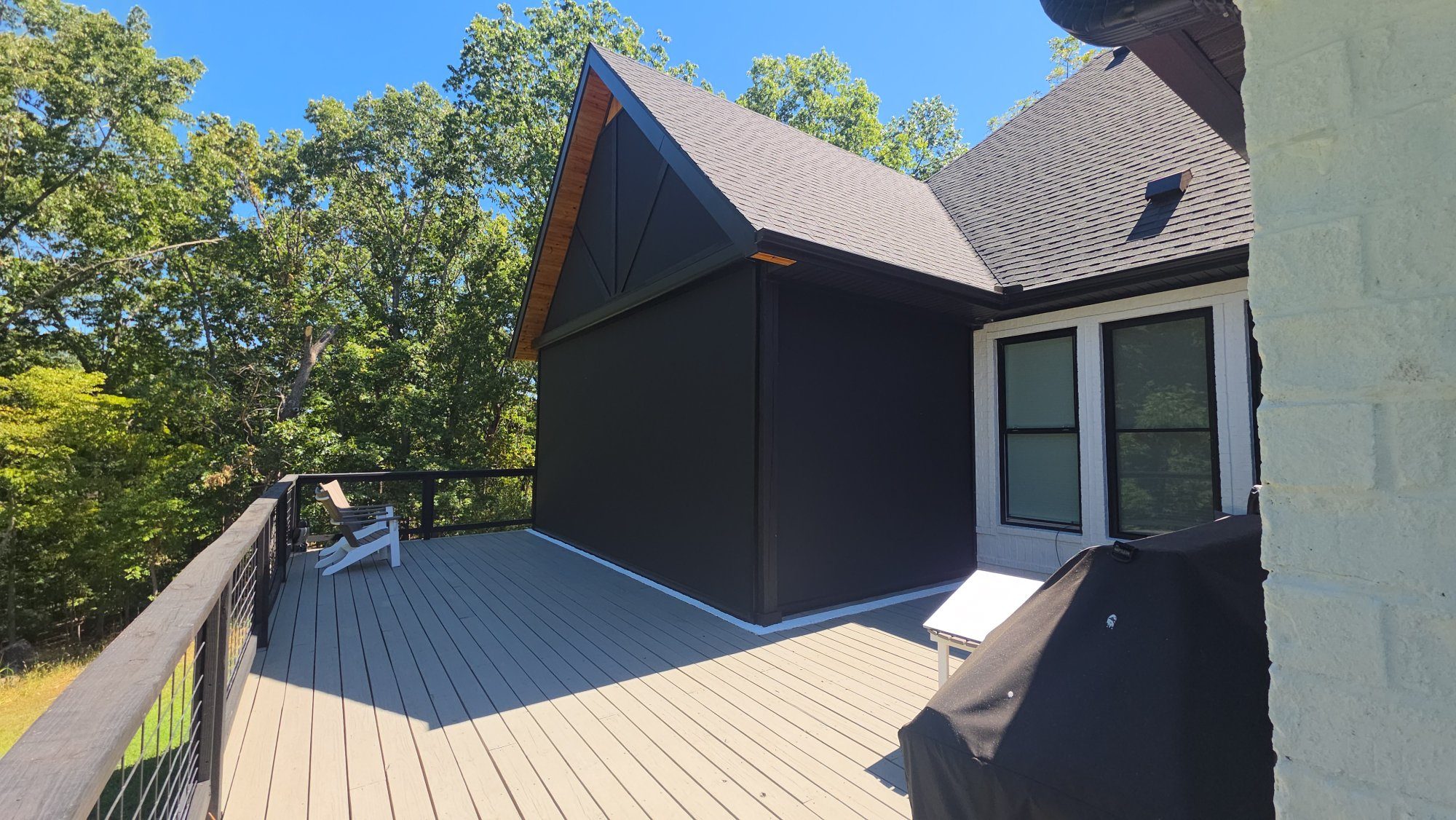 Flat black motorized retractable screens fully deployed enclosing a covered deck in Rogers, Arkansas — cedar gable accent, black cable railing, installed by NWA Security Shutters