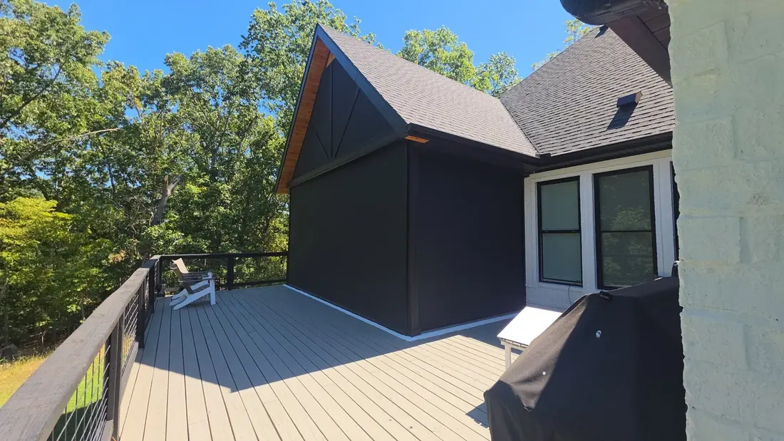 Flat black motorized retractable screens fully deployed enclosing a covered deck in Rogers, Arkansas — cedar gable accent, black cable railing, installed by NWA Security Shutters